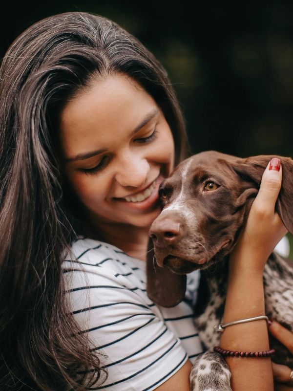 A person smiling while holding a brown and white spotted dog with floppy ears.