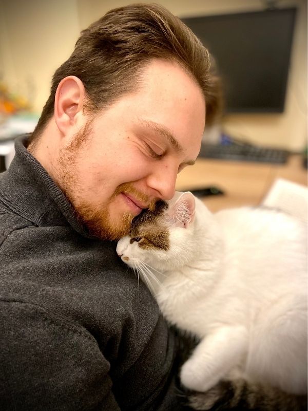 A person with closed eyes affectionately nuzzles a white cat with brown markings on its head.
